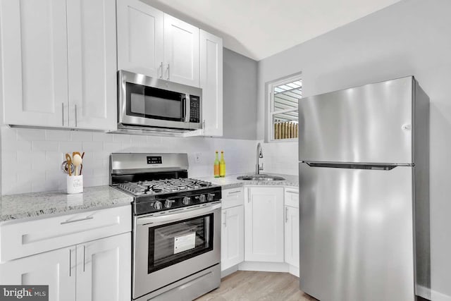 kitchen with white cabinets, stainless steel appliances, sink, and light stone counters