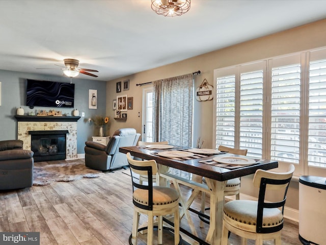 dining area featuring a fireplace, light wood-type flooring, ceiling fan, and plenty of natural light