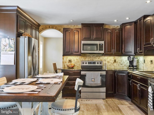 kitchen with dark brown cabinets, appliances with stainless steel finishes, light hardwood / wood-style floors, and backsplash