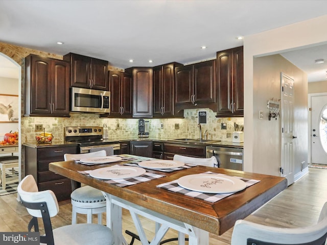 kitchen with backsplash, appliances with stainless steel finishes, dark brown cabinetry, sink, and light hardwood / wood-style flooring