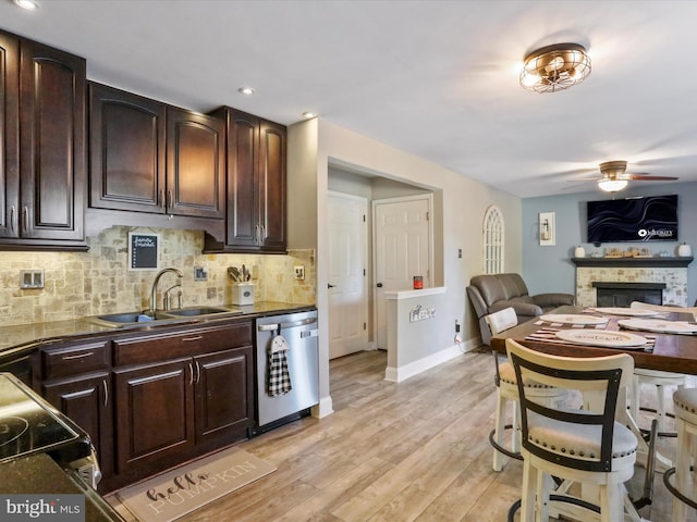 kitchen featuring a fireplace, light wood-type flooring, sink, dishwasher, and ceiling fan