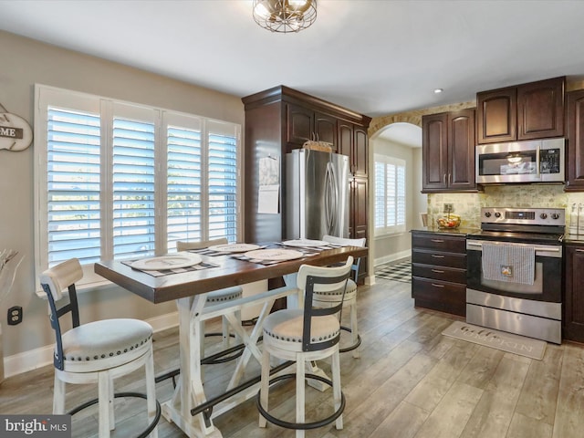 kitchen with decorative backsplash, dark brown cabinetry, light hardwood / wood-style floors, and stainless steel appliances