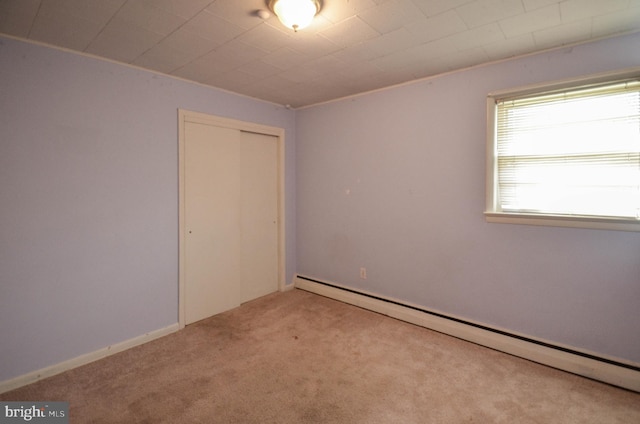 carpeted empty room featuring a baseboard heating unit