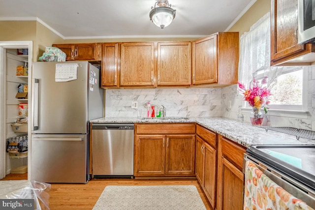 kitchen with sink, stainless steel appliances, light stone counters, light hardwood / wood-style flooring, and crown molding