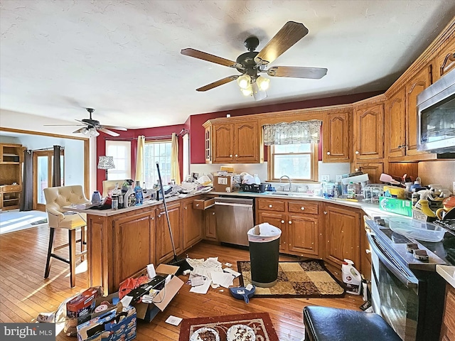 kitchen featuring a breakfast bar, kitchen peninsula, ceiling fan, light wood-type flooring, and stainless steel appliances