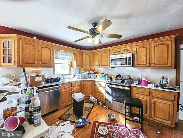 kitchen with ceiling fan, sink, stainless steel appliances, and light hardwood / wood-style floors