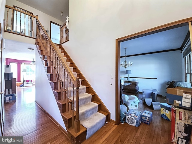 staircase featuring wood-type flooring, ceiling fan with notable chandelier, and ornamental molding