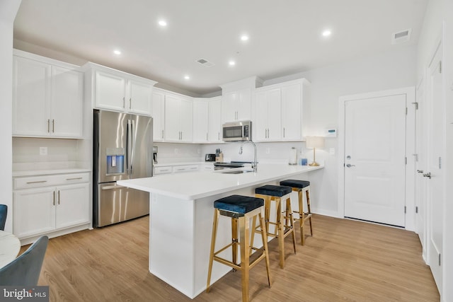 kitchen with kitchen peninsula, appliances with stainless steel finishes, light wood-type flooring, a breakfast bar, and white cabinetry