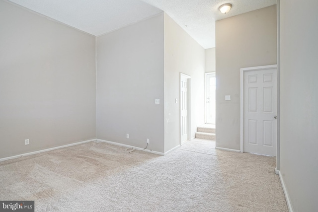 carpeted empty room with high vaulted ceiling and a textured ceiling