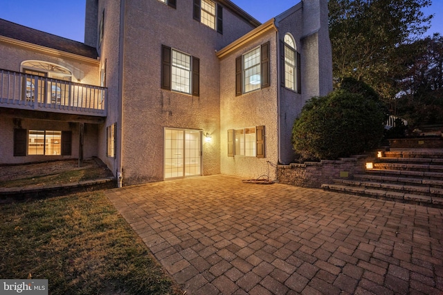 back house at dusk featuring a balcony and a patio area