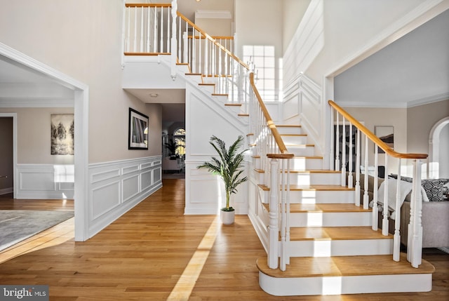 stairs with a towering ceiling, ornamental molding, and hardwood / wood-style flooring