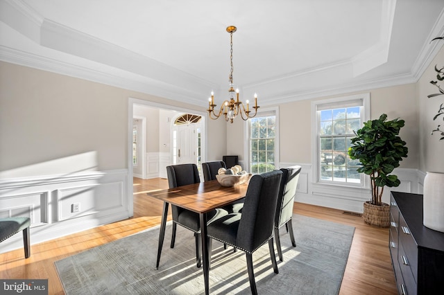 dining space with ornamental molding, light hardwood / wood-style floors, a notable chandelier, and a tray ceiling