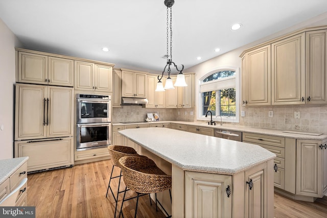 kitchen featuring cream cabinets, stainless steel appliances, light wood-type flooring, decorative light fixtures, and a center island