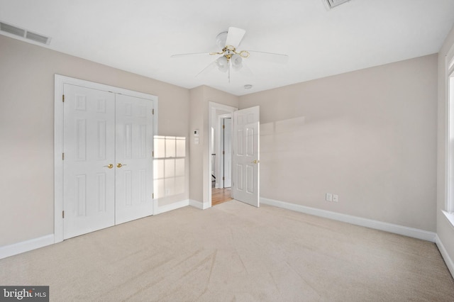 unfurnished bedroom featuring a closet, multiple windows, light colored carpet, and ceiling fan