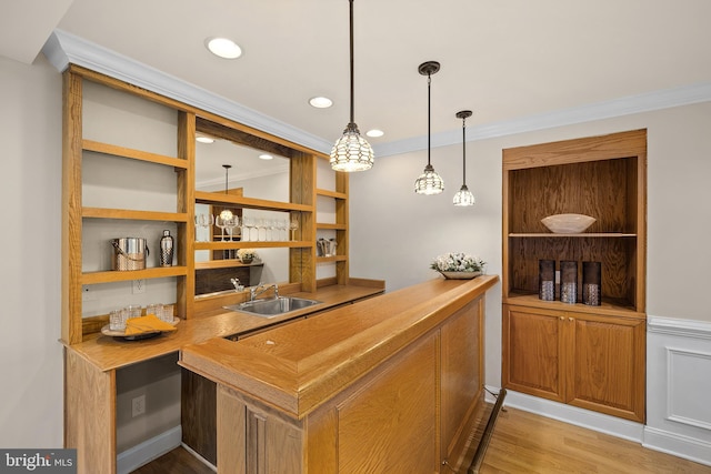 bar featuring light wood-type flooring, hanging light fixtures, sink, and ornamental molding