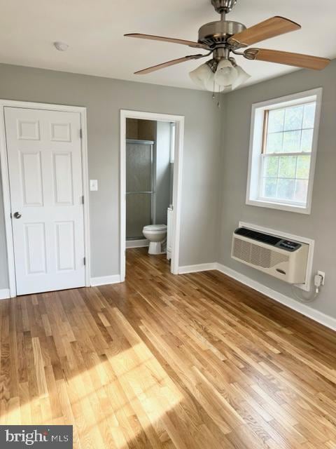 unfurnished bedroom with a wall mounted air conditioner, light wood-type flooring, ensuite bathroom, and ceiling fan