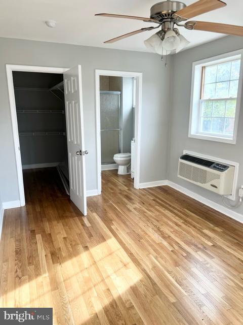 unfurnished bedroom featuring a wall mounted AC, ensuite bathroom, and light hardwood / wood-style flooring