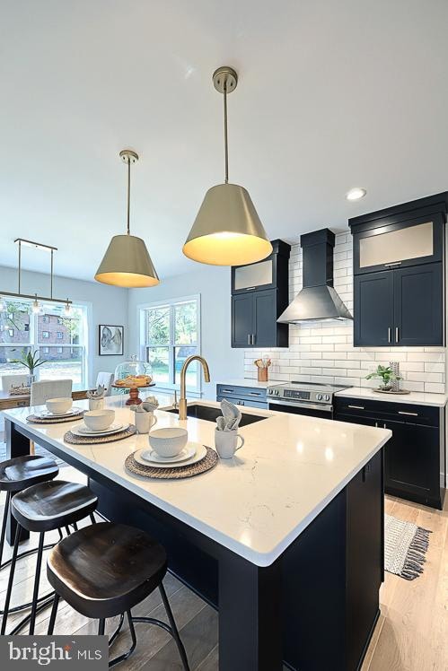 kitchen featuring wall chimney exhaust hood, a breakfast bar area, an island with sink, and stainless steel electric stove