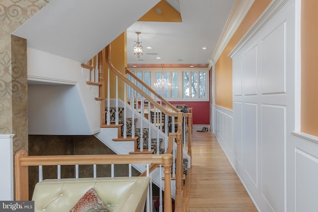 stairs featuring wood-type flooring, crown molding, and an inviting chandelier