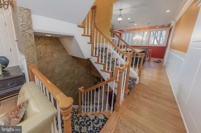 stairs with ornamental molding, wood-type flooring, and a notable chandelier