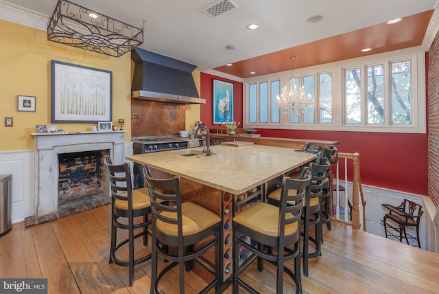 kitchen featuring ornamental molding, sink, wall chimney range hood, light hardwood / wood-style floors, and hanging light fixtures