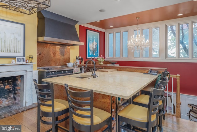 kitchen featuring decorative backsplash, wall chimney exhaust hood, sink, decorative light fixtures, and light hardwood / wood-style flooring