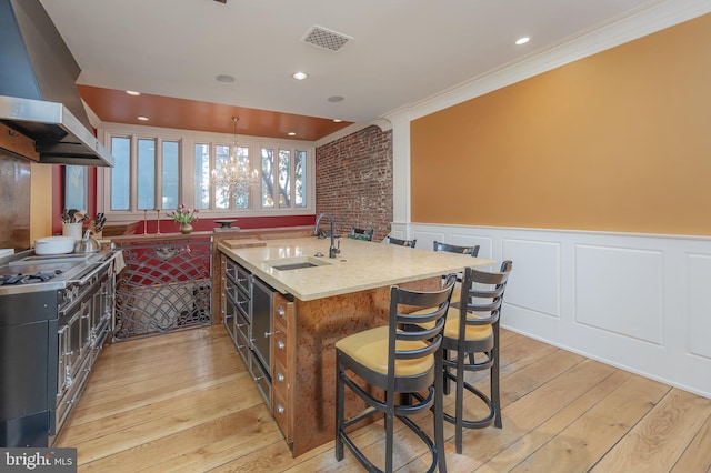 kitchen featuring a breakfast bar, sink, light stone countertops, range hood, and light hardwood / wood-style floors