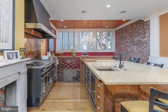 kitchen featuring sink, wall chimney exhaust hood, light stone countertops, ornamental molding, and decorative light fixtures