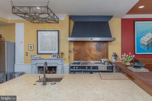 kitchen featuring crown molding, wall chimney range hood, sink, and appliances with stainless steel finishes