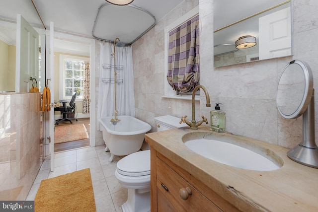 bathroom featuring tile patterned flooring, a tub to relax in, toilet, vanity, and tile walls