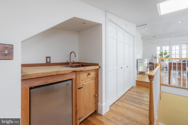 kitchen featuring stainless steel fridge, light hardwood / wood-style floors, sink, and wooden counters