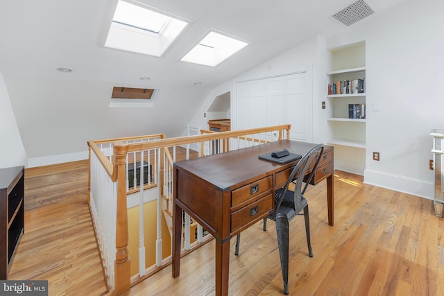 office with light hardwood / wood-style floors, lofted ceiling with skylight, and built in features