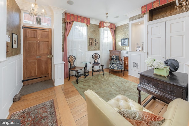 entryway with a notable chandelier, decorative columns, crown molding, and light hardwood / wood-style flooring