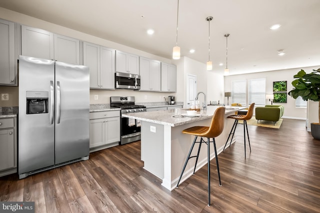 kitchen with stainless steel appliances, pendant lighting, a kitchen island with sink, and dark hardwood / wood-style flooring