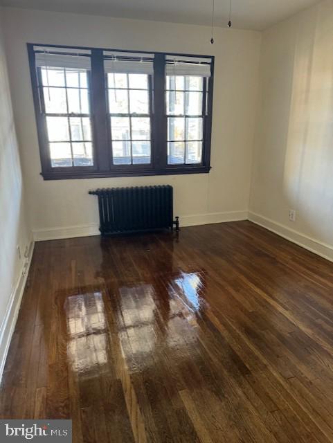 unfurnished room featuring a wealth of natural light, dark hardwood / wood-style floors, and radiator heating unit