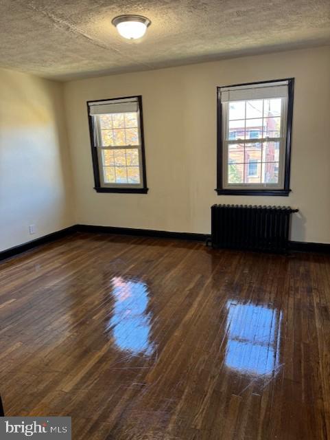 empty room with plenty of natural light, radiator heating unit, and dark hardwood / wood-style flooring