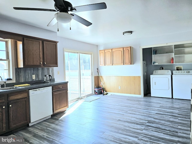 kitchen featuring washer and clothes dryer, dark brown cabinets, white dishwasher, wooden walls, and dark wood-type flooring