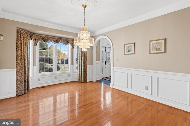 unfurnished dining area featuring a notable chandelier, crown molding, visible vents, wainscoting, and arched walkways