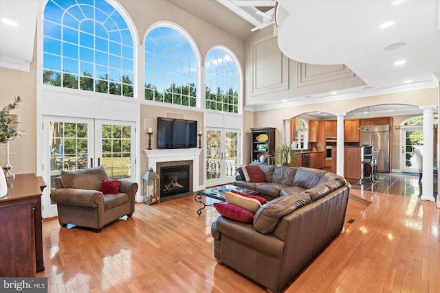 living area with light wood-style flooring, ornate columns, ornamental molding, a glass covered fireplace, and a high ceiling