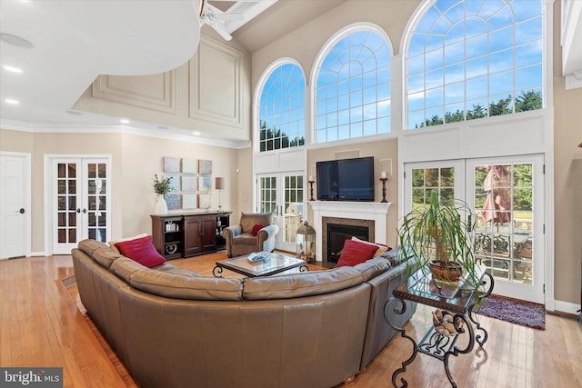 living room with crown molding, light wood-style floors, french doors, and a fireplace