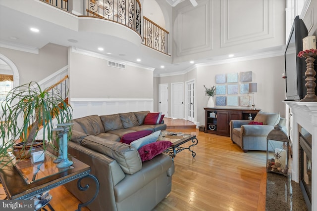 living area with a glass covered fireplace, visible vents, a high ceiling, and crown molding