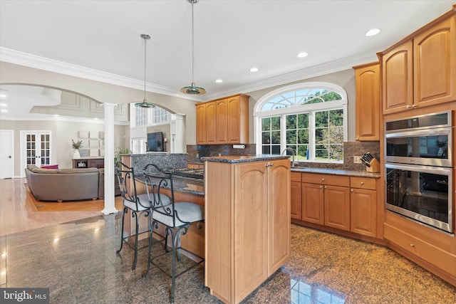 kitchen featuring decorative columns, stainless steel double oven, granite finish floor, and ornamental molding