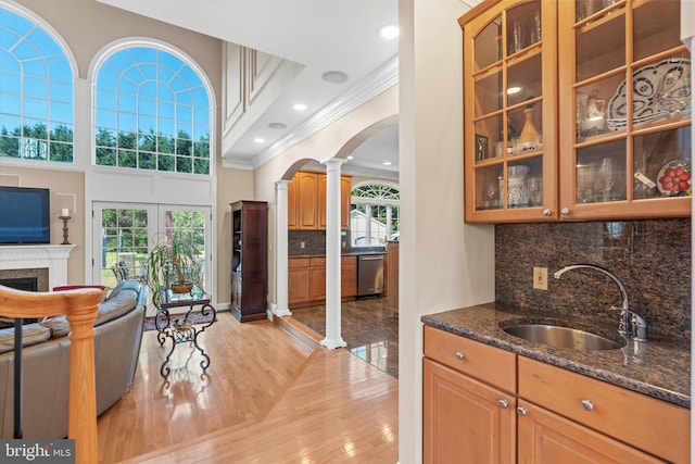 bar featuring arched walkways, dishwasher, a sink, ornamental molding, and ornate columns