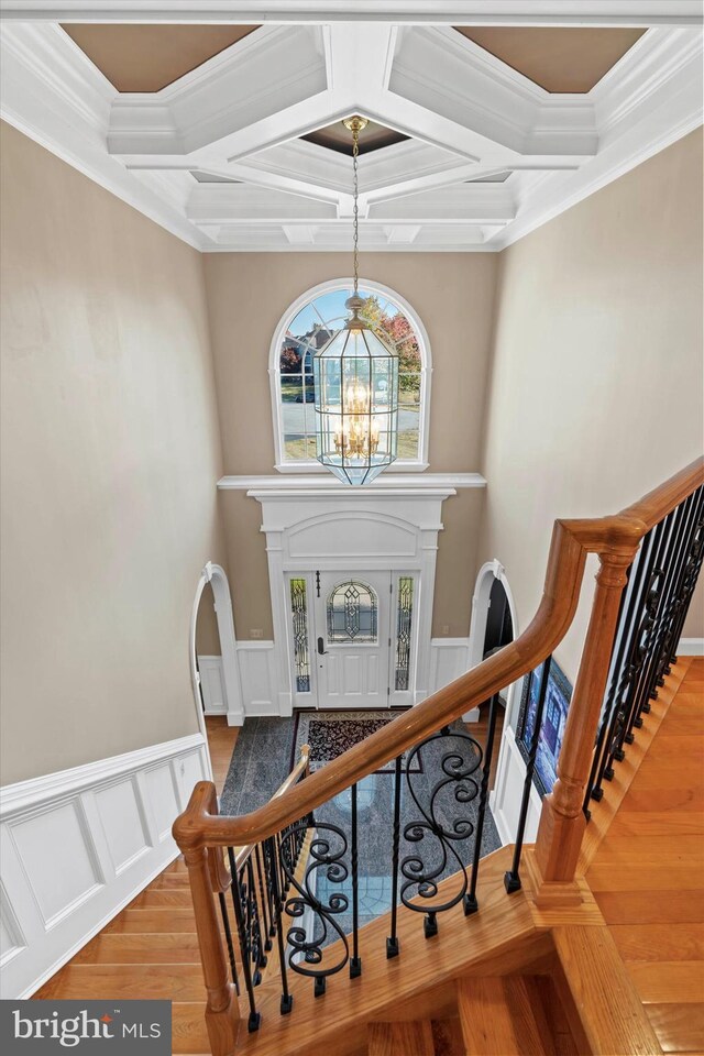 stairs featuring coffered ceiling, a chandelier, wood finished floors, and ornamental molding