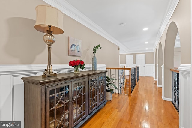 corridor with a decorative wall, ornamental molding, light wood-type flooring, an upstairs landing, and a wainscoted wall