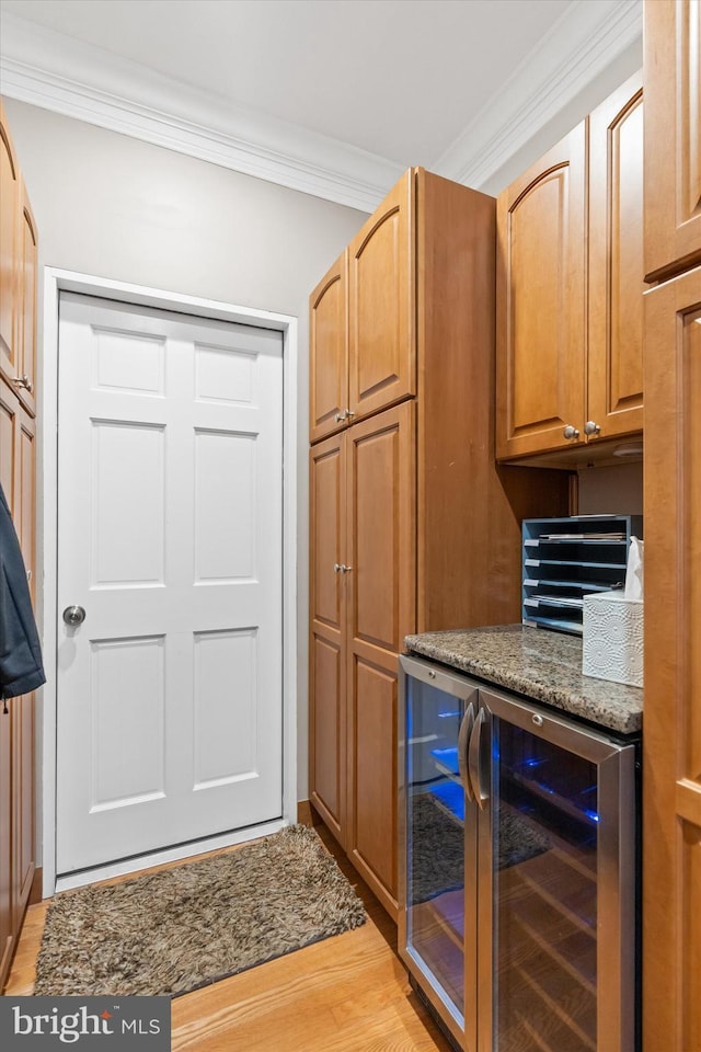 kitchen featuring wine cooler, stone counters, light wood finished floors, and crown molding
