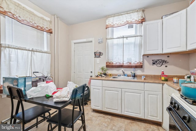 kitchen featuring white range with gas cooktop, sink, and white cabinets