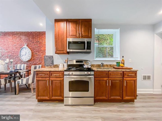 kitchen featuring light wood-type flooring, appliances with stainless steel finishes, sink, and light stone countertops