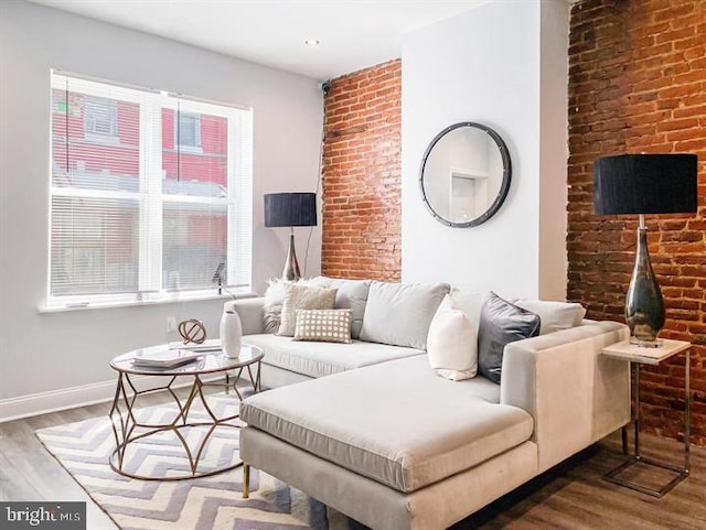 living room featuring wood-type flooring, plenty of natural light, and brick wall