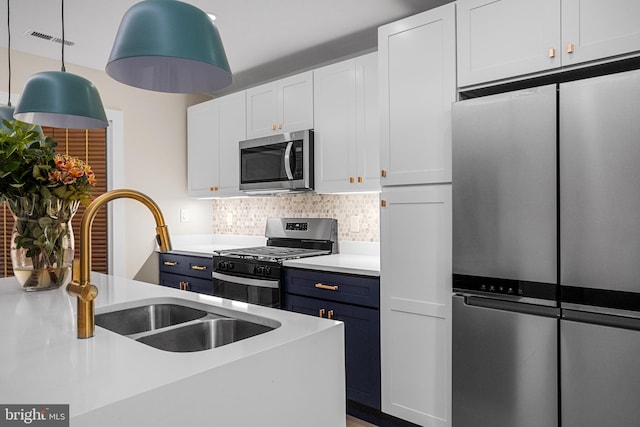 kitchen with tasteful backsplash, blue cabinetry, appliances with stainless steel finishes, pendant lighting, and white cabinets